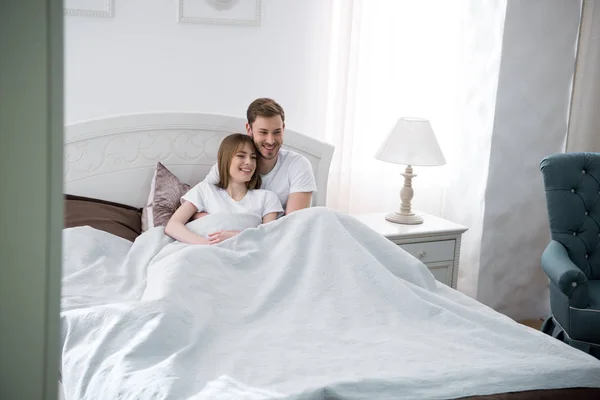 Молодой мужчина обнимает свою девушку в спальне с современным интерьером — стоковое фото