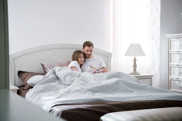 Couple lying and reading book in modern bedroom — Stock Photo