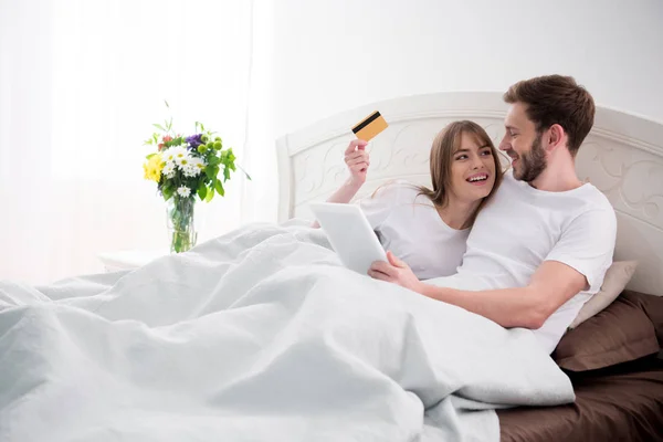 Пара делает онлайн покупки, лежа в уютной современной спальне — стоковое фото