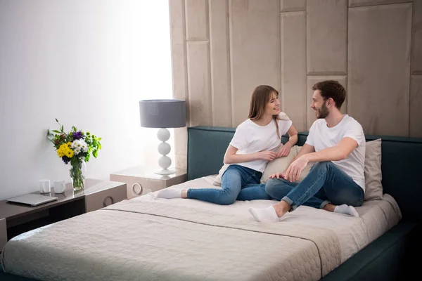Casal feliz sentado na cama no quarto moderno acolhedor — Fotografia de Stock