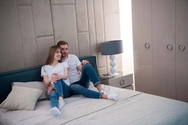Jovem casal sentado na cama com travesseiros no quarto moderno — Fotografia de Stock