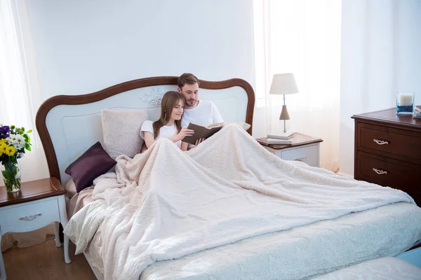 Libro de lectura de pareja bajo manta en dormitorio moderno — Stock Photo