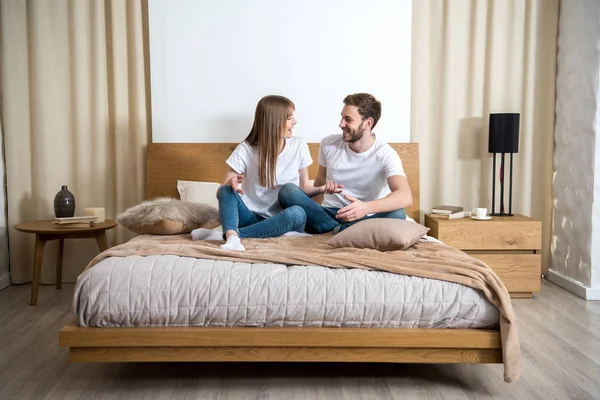 Casal sorridente conversando e sentado na cama no quarto moderno acolhedor — Fotografia de Stock