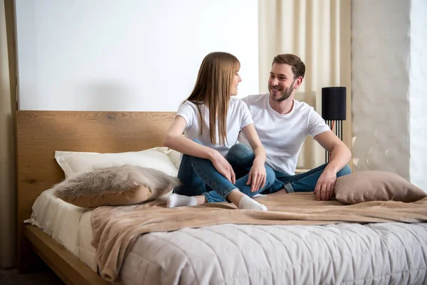 Молода пара сидить у ліжку з подушками в сучасній спальні — стокове фото