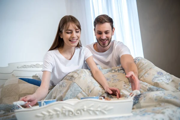 Casal na cama com café da manhã na bandeja no quarto moderno — Fotografia de Stock
