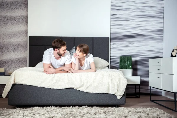 Pareja feliz mintiendo y hablando en acogedor dormitorio moderno - foto de stock