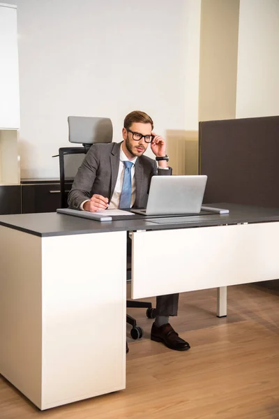 Молодий бізнесмен використовує ноутбук, сидячи за столом в офісі — стокове фото