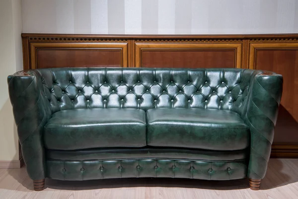 Sofá de couro verde na frente da parede com decoração de madeira — Fotografia de Stock