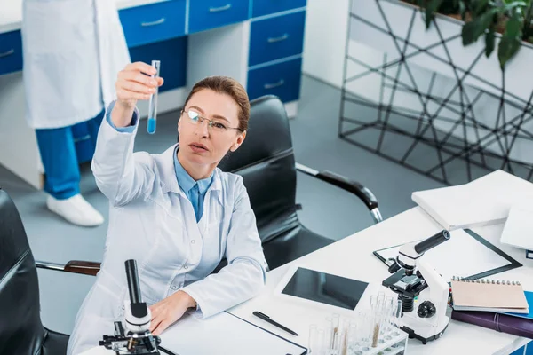 Selective focus of female researcher looking at tube with reagent in hand with colleague behind in lab — Stock Photo