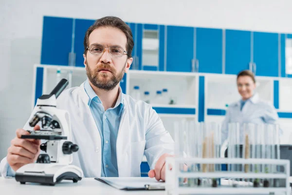 Selective focus of scientist in white coat and eyeglasses at workplace with microscope in laboratory — Stock Photo