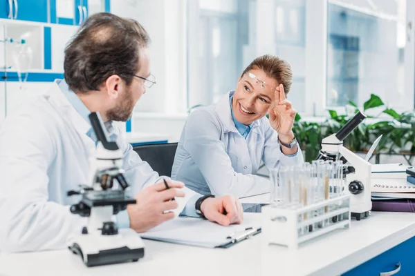 Investigadores científicos en batas blancas que trabajan juntos en el lugar de trabajo en laboratorio - foto de stock