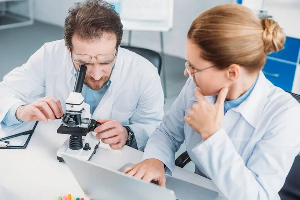 Portrait of scientific researchers in white coats working together at workplace with microscope  in laboratory — Stock Photo