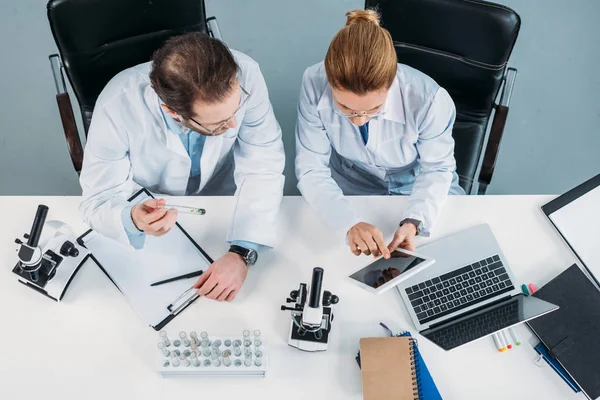 Вид зверху наукових дослідників у білих пальто з використанням таблеток разом на робочому місці в лабораторії — стокове фото