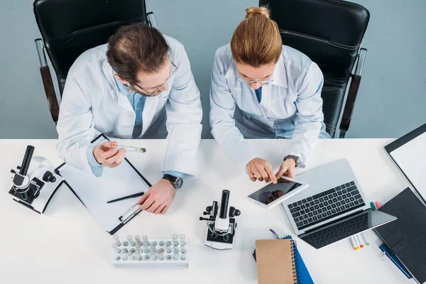 Vista aérea de los investigadores científicos en batas blancas que utilizan tabletas juntas en el lugar de trabajo en el laboratorio - foto de stock