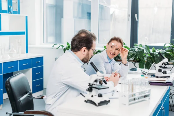 Científicos en batas de laboratorio y anteojos discutiendo el trabajo en el lugar de trabajo en el laboratorio - foto de stock