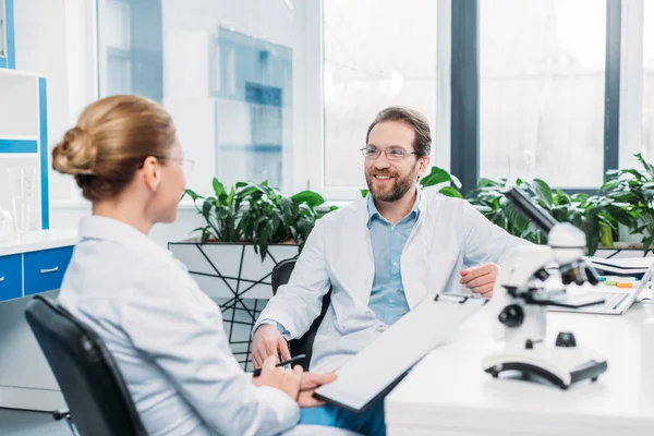 Scientists in lab coats and eyeglasses discussing work at workplace in lab — Stock Photo