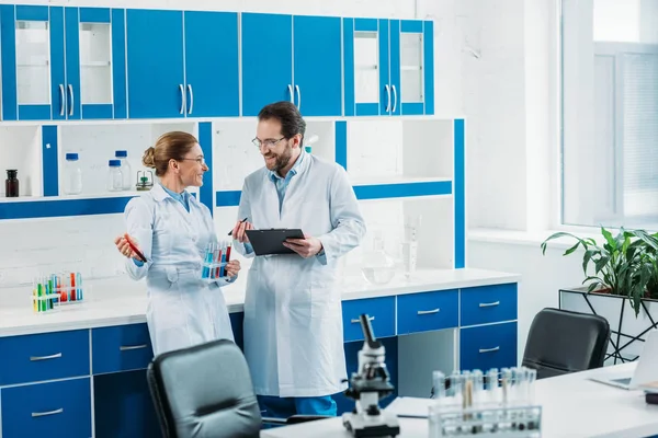 Scientific researchers in white coats and eyeglasses with flasks and notepad in laboratory — Stock Photo
