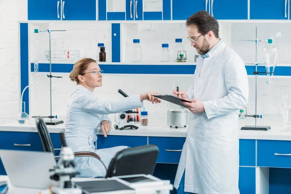 Scientific researchers in white coats and eyeglasses working together in laboratory — Stock Photo