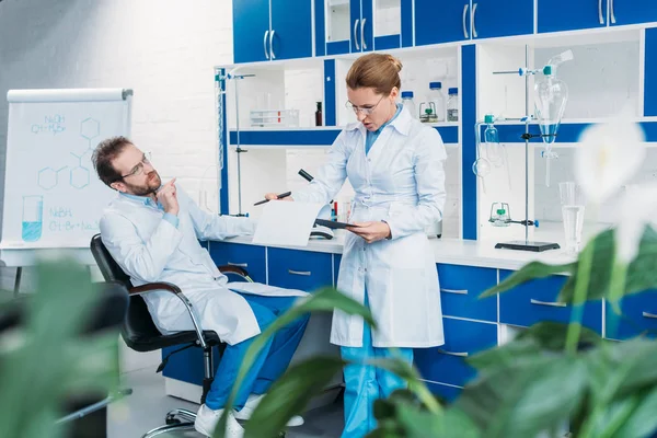 Scientific researchers in white coats discussing work together in laboratory — Stock Photo