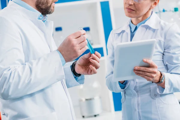 Plan recadré de scientifiques en blouse blanche avec tube avec réactif et comprimé en laboratoire — Photo de stock