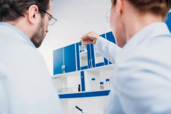 Vue arrière des scientifiques en blouse blanche regardant tube avec réactif en laboratoire — Photo de stock