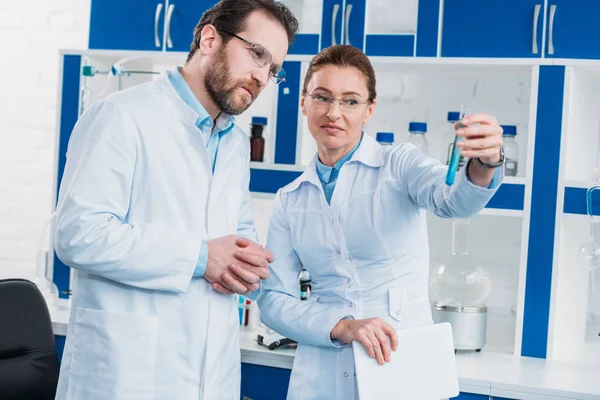 Retrato de científicos en anteojos mirando tubo con reactivo en laboratorio - foto de stock