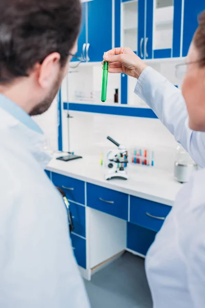 Back view of scientists looking at tube with reagent in laboratory — Stock Photo