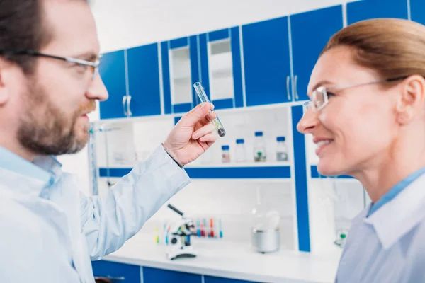 Vista lateral de científicos en anteojos con tubo con reactivo en laboratorio - foto de stock