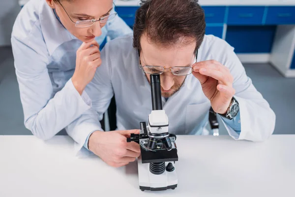 Científicos con batas blancas y anteojos que trabajan juntos con reactivos en laboratorio - foto de stock