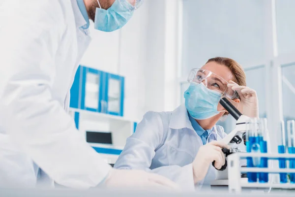 Científicos en batas blancas, guantes médicos y gafas haciendo investigación científica juntos en laboratorio - foto de stock
