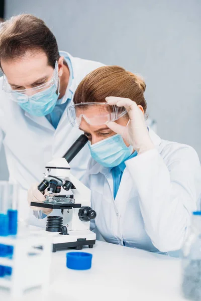 Scientifiques en blouse blanche, gants médicaux et lunettes faisant de la recherche scientifique ensemble en laboratoire — Photo de stock