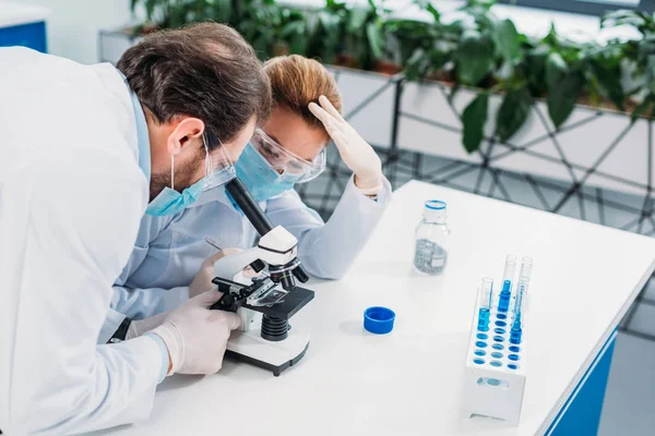 Учёные в белых халатах, медицинских перчатках и очках совместно проводят научные исследования в лаборатории — стоковое фото
