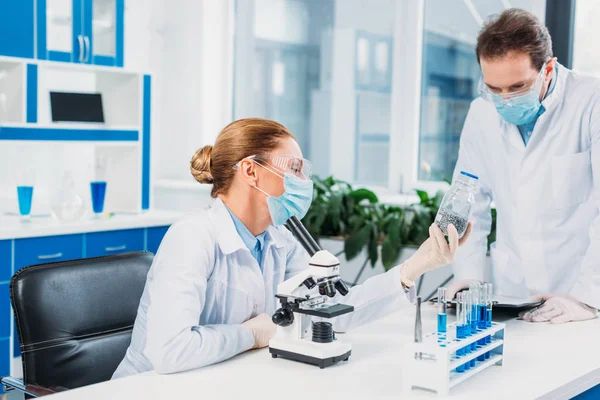 Scientists in white coats and goggles working with reagents and microscope in laboratory — Stock Photo