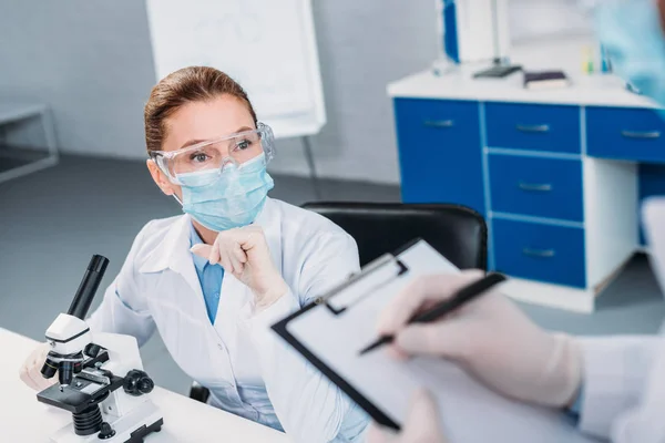 Частковий погляд вчених у медичних масках та окулярах, що працюють над науковими дослідженнями в лабораторії — стокове фото