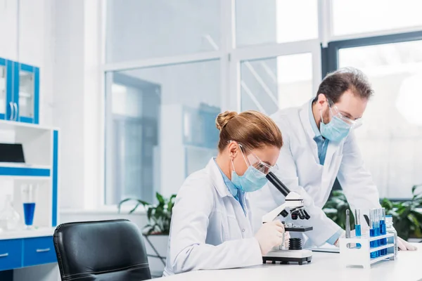 Scienziati in maschere e occhiali medici che lavorano alla ricerca scientifica in laboratorio — Foto stock