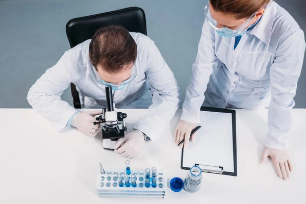 Overhead view of scientists in medical masks and goggles working on scientific research in laboratory — Stock Photo