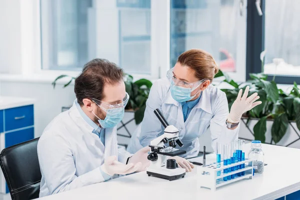 Científicos en máscaras médicas y gafas que trabajan en la investigación científica en laboratorio - foto de stock