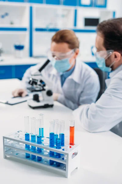 Focalisation sélective des tubes avec des réactifs et des scientifiques sur le lieu de travail en laboratoire — Photo de stock