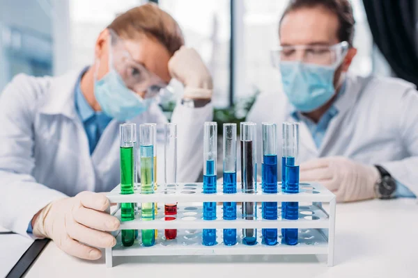 Selective focus of scientific researchers in goggles and medical masks looking at reagents in tubes in lab — Stock Photo