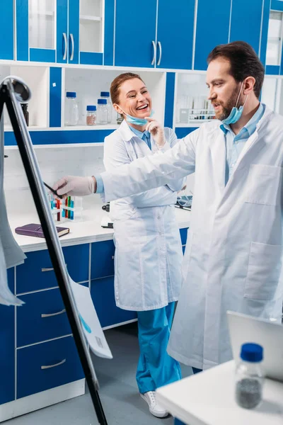 Wissenschaftler in weißen Mänteln in der Nähe der Tafel für Notizen, die während der Arbeit im Labor diskutiert werden — Stockfoto