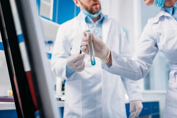 Cropped shot of scientists in white coats with tube in lab — Stock Photo