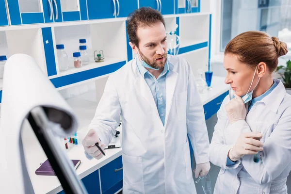 Scienziato in camici bianchi vicino all'asse per appunti che discutono durante il lavoro in laboratorio — Foto stock