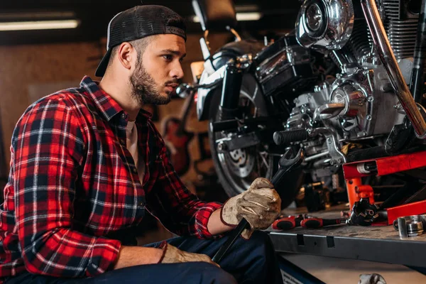 Hermosa estación de reparación de bicicletas trabajador con llave inglesa mirando la motocicleta - foto de stock