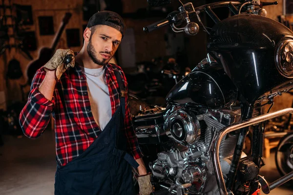 Handsome bike repair station worker with wrench in front of motorcycle — Stock Photo