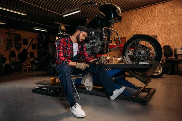 Müder Mitarbeiter einer Fahrradwerkstatt sitzt mit Schraubenschlüssel vor Motorrad — Stockfoto