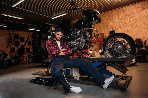 Bike repair station worker sitting in front of motorcycle at garage — Stock Photo