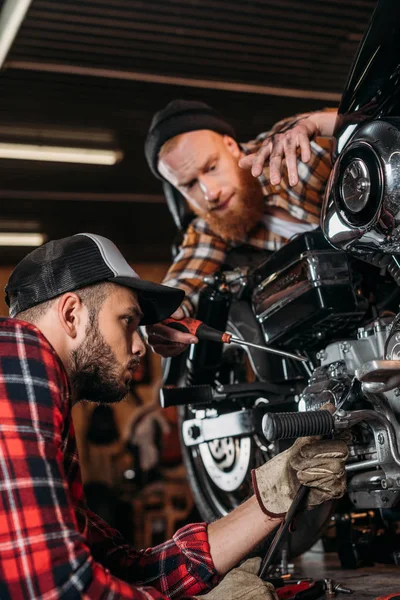 Handsome young mechanics repairing motorcycle together at garage — Stock Photo