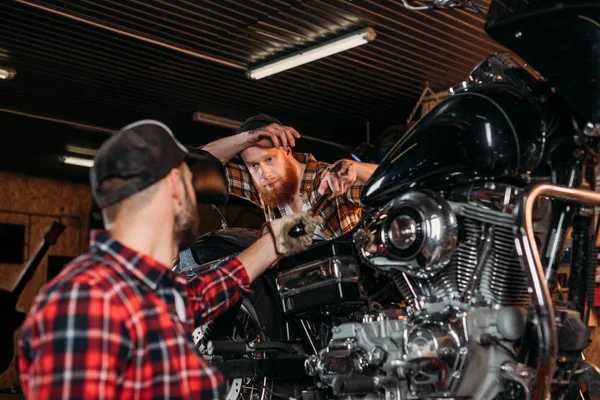 Mecánicos guapos reparación de motocicletas juntos en el garaje personalizado - foto de stock