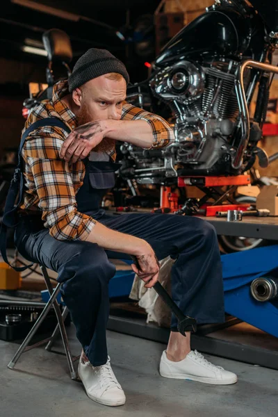 Tired bike repair station worker wiping face of sweat after work at garage — Stock Photo