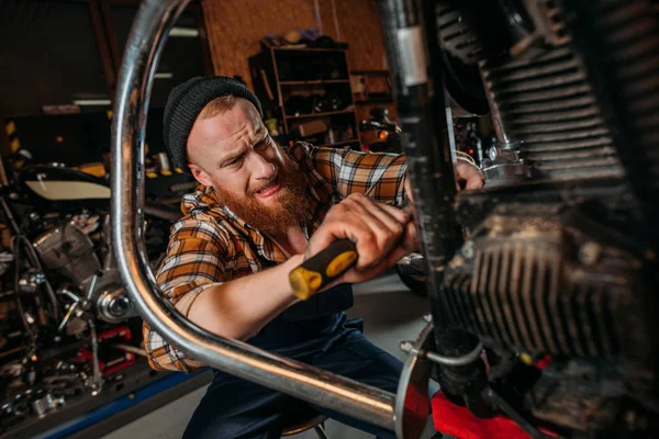 Emotional bike repair station worker using screwdriver to fix motorcycle at garage — Stock Photo